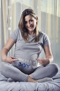快乐的未来妈妈微笑着，在她怀孕的肚子上显示标志
