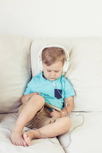 3 年岁的男孩坐在沙发上，听听音乐。小小的可爱的男孩，看动画片的电话。小男孩