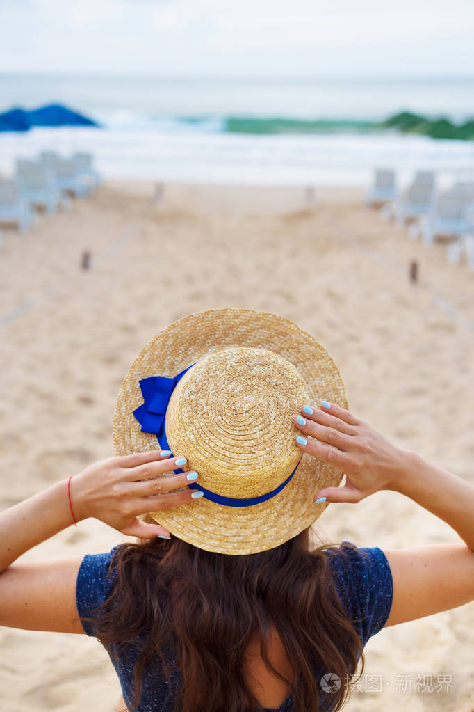 美丽的女孩在一顶帽子坐在沙滩上