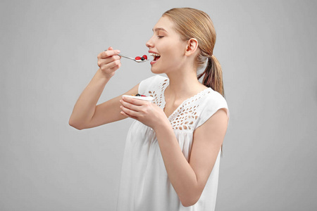 年轻女子在浅色背景上吃酸奶