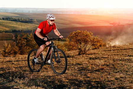 明亮的年轻男子在山地自行车骑在秋季景观