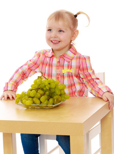 漂亮的白人女孩吃葡萄坐在桌前