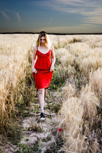漂亮的金发女郎，在红色的连衣裙，在日落时的麦田