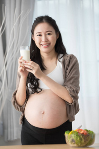 亚洲孕妇在厨房与健康的蔬菜和牛奶