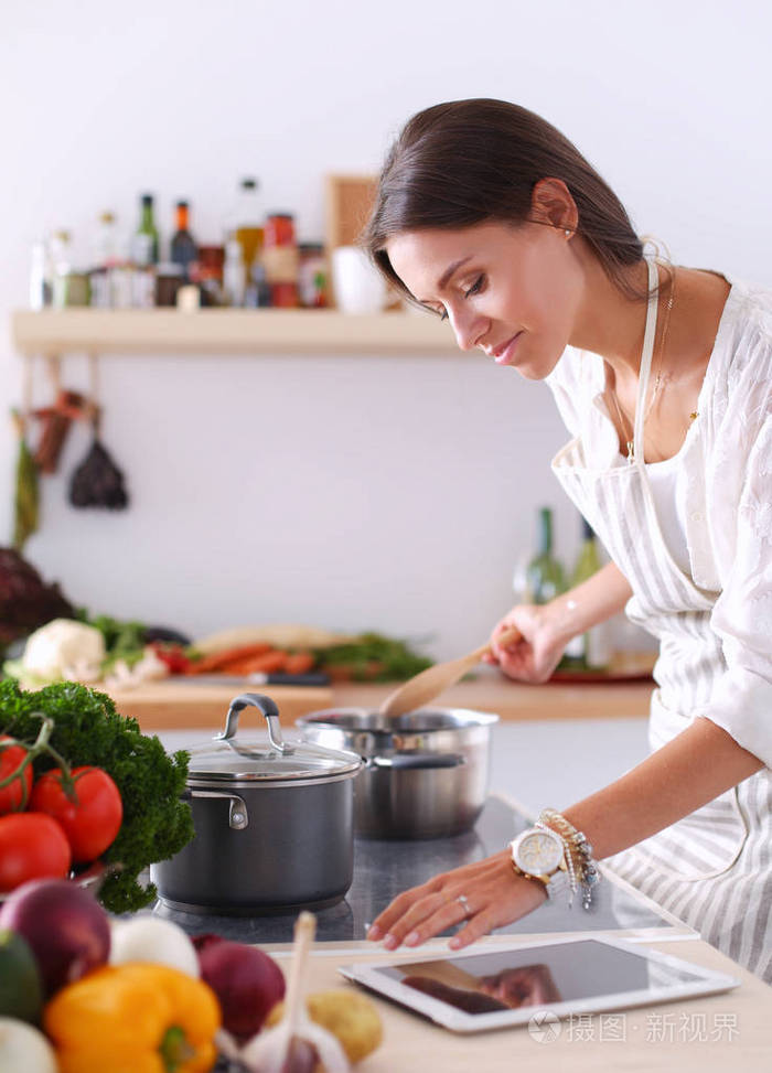使用一台平板电脑,在她的厨房里做饭的年轻女人