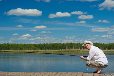 人在一顶帽子和一件白衬衫，是在湖上捕鱼