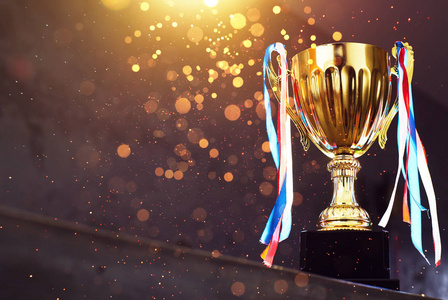 低调的金色奖杯在模糊的灰色背景与抽象闪亮的灯光照片