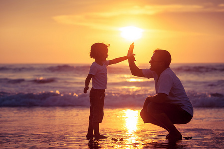 父亲和儿子在日落的时候在海滩上玩照片