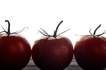 三只红色的西红柿站在一排黑色的木桌上反对白色背景特写。西红柿的剪影概念