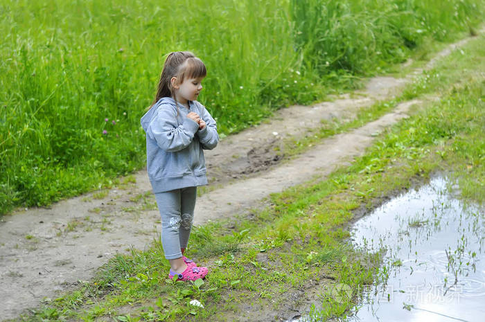 橡胶鞋的小女孩在水坑在夏季森林附近许愿