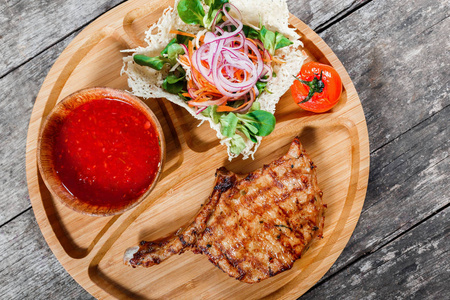 烤的牛肉牛排上骨 新鲜的沙拉 烤的蔬菜和番茄酱涂在切菜板上木制的背景。热的肉菜。顶视图