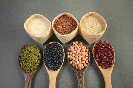 谷物和种子豆 黑豆 红豆 花生 绿豆 泰国香米 糙米和白米饭 有益健康的木勺子在灰色的背景