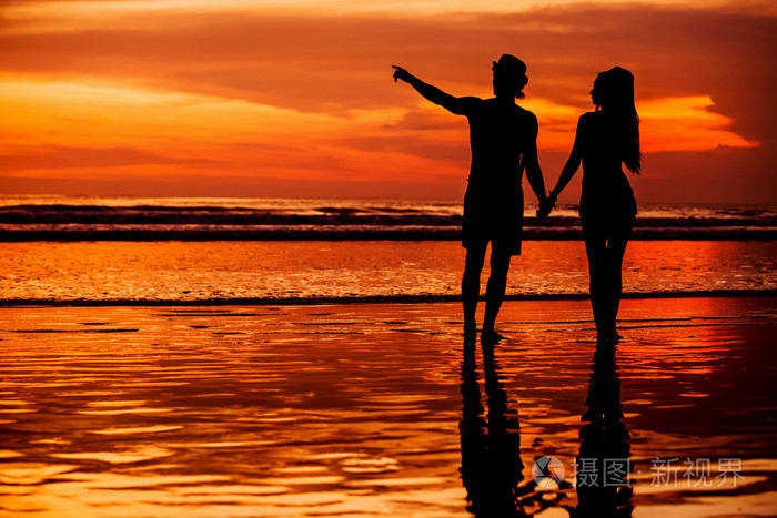 对年轻夫妇的剪影爱好不容易才开始在沙滩上美丽夕阳红为背景