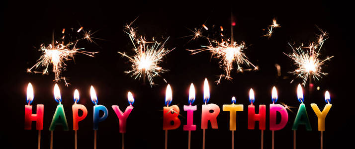 五颜六色的快乐生日蜡烛用烟火烟花,在黑色的背景上照片