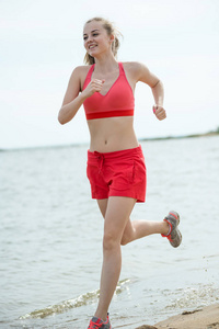 年轻的女士在阳光灿烂的夏天砂沙滩上运行。锻炼。慢跑