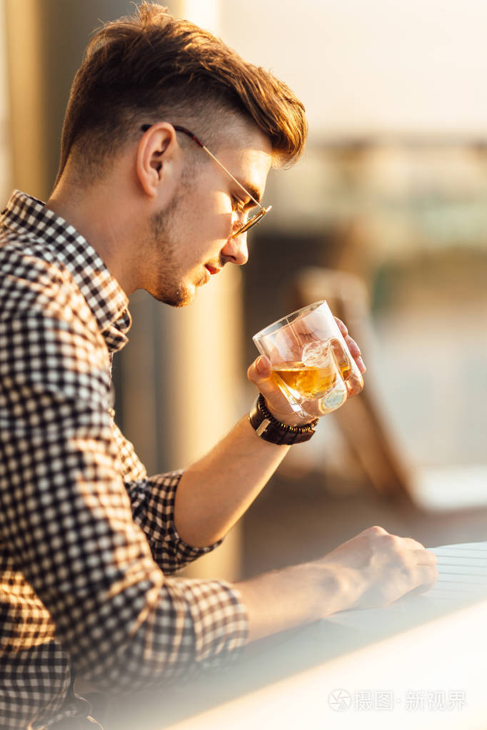 时尚的男人坐在表和喝威士忌