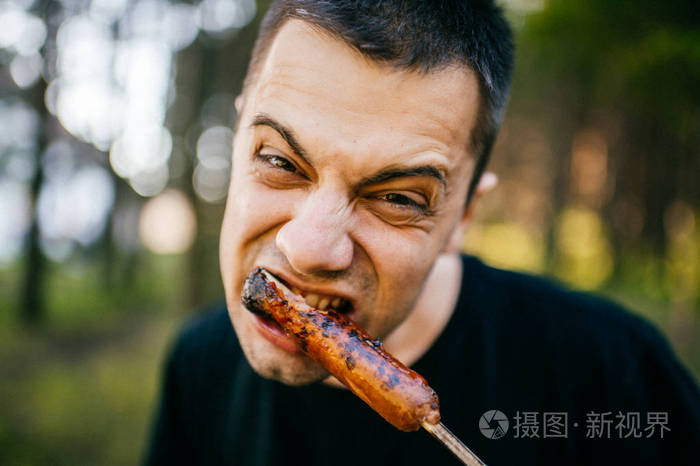 与男性舔咬的特写肖像烤香肠的恶心丑陋可怕的面部表情.肉的情人.