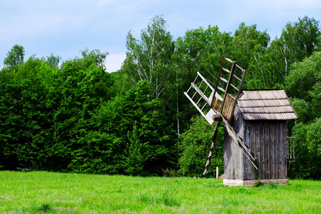 古老的木制风车在绿色的田野 森林和蓝色天空背景