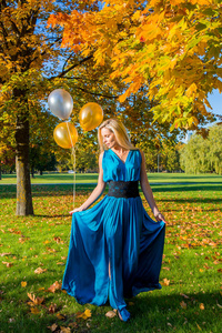 美丽的年轻的女士穿着礼服站在公园在金色的秋季季节在她的手气球