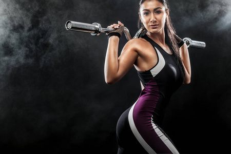 运动的漂亮女子与杠铃使健身运动在黑色背景下保持健康