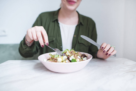 女孩的手用餐具在一盘沙拉上。一个女孩用叉子和刀子吃沙拉。健康饮食