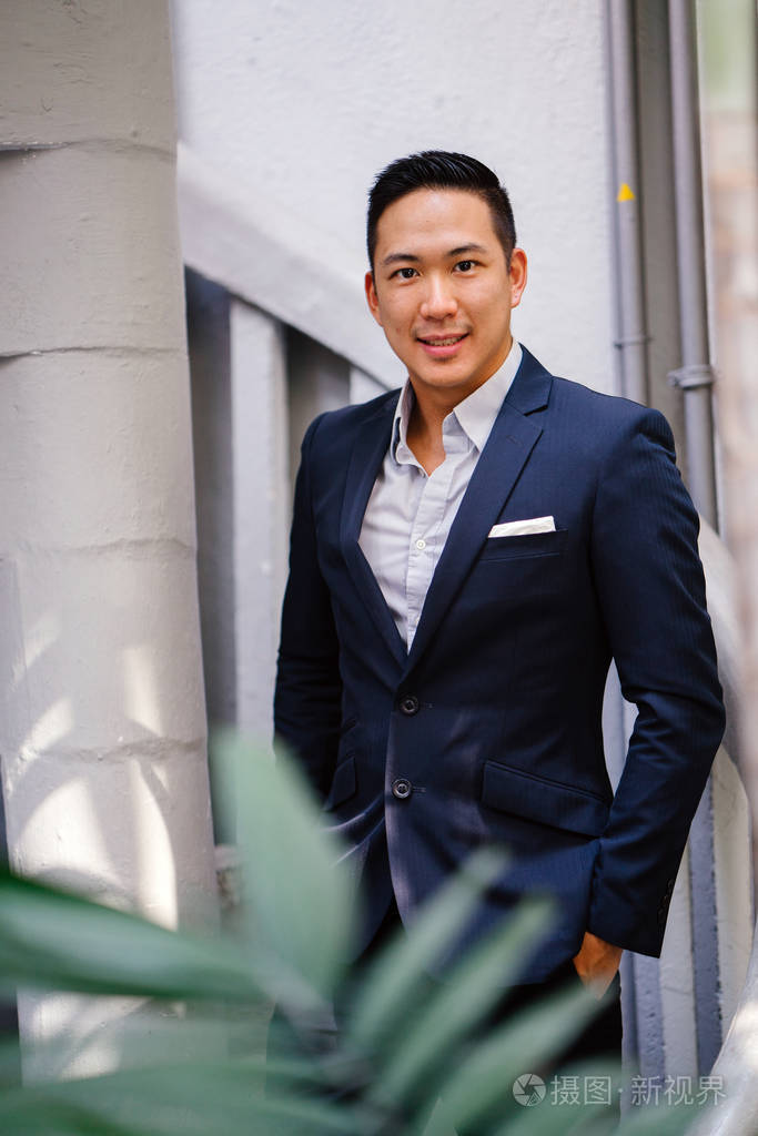 一个英俊, 年轻, 聪明的中国亚裔男子的肖像微笑着, 站在绿色的墙上的