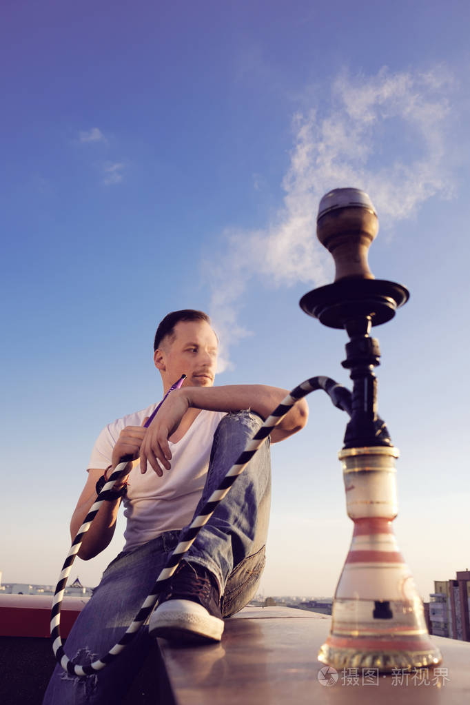 男子在日落时在楼顶上吸烟水烟