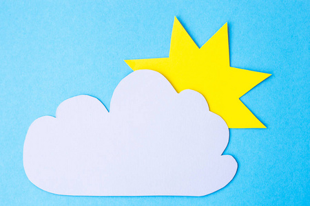 黄色的纸太阳旁边的灰色云在蓝色的背景。多云天气概念