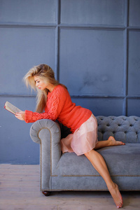 妇女在家坐在现代椅子在窗口前面放松在她的客厅读书书