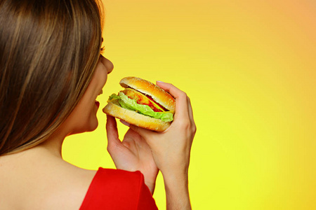 在黄色背景的红色礼服藏品汉堡的美丽的妇女的后面看法