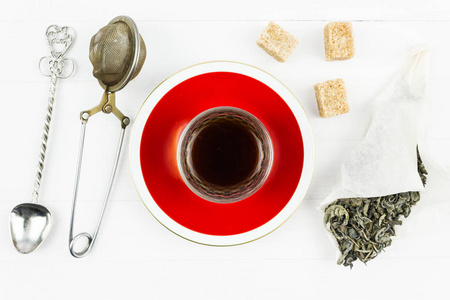 一杯茶放在一张白色桌子上的红碟上。甘蔗糖和一串干绿茶