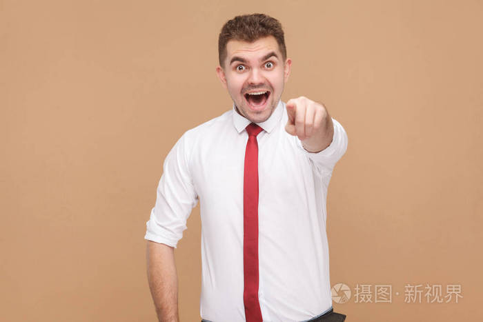 快乐的商人指着手指在镜头和微笑的浅褐色背景