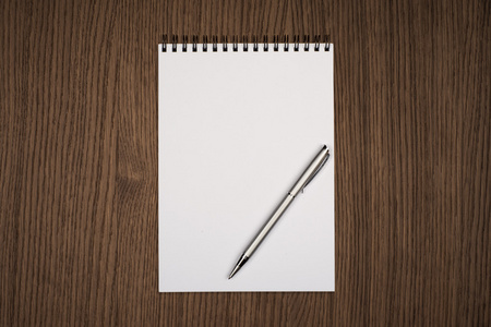 空白记事本与办公室木制的桌子上的钢笔