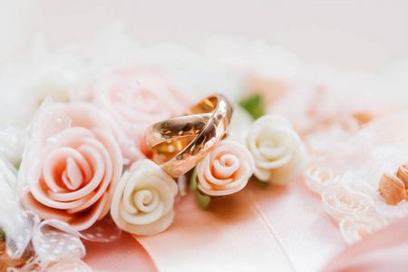 一对金色的结婚戒指花边织物与玫瑰和弓。婚礼纺织品细节。爱情与婚姻的象征