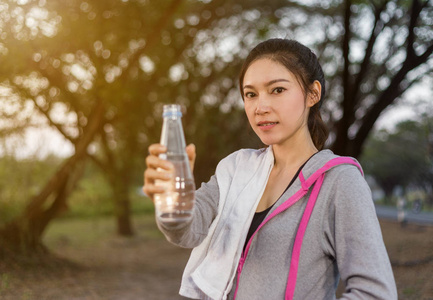 年轻运动妇女与瓶水在公园里