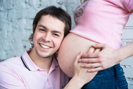 怀孕的夫妇抱着女人的肚子，关闭了开心的笑容丈夫听 thr 孕妇肚皮