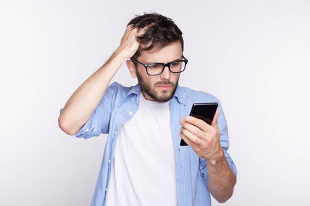 疲倦的男学生白读文章 做工作搜索信息在互联网使用他的智能手机上孤立的画像。麻烦的人，使情绪面部表情的研究