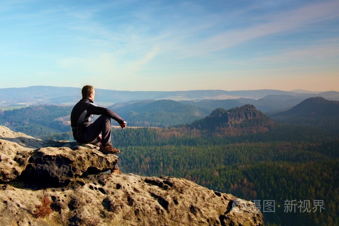 寂寞的时刻.男人坐在岩石和观看到多彩雾,雾中森林谷峰
