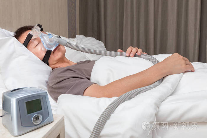 中年亚裔男子睡在他床上,穿着 cpap 面罩连接