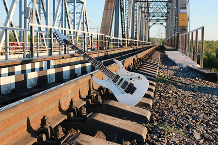 在铁轨和石头上的白色电吉他。