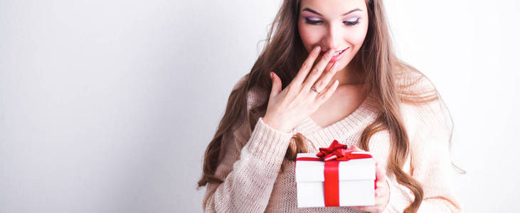 年轻女人幸福的微笑举行礼品盒在手中，站在灰色的背景