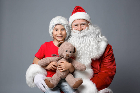 可爱的小男孩与泰迪熊坐在圣诞老人的膝上反对颜色背景