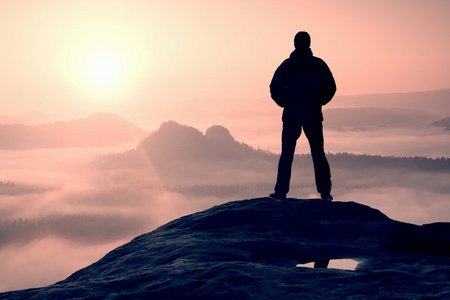 独自徒步旅行者站在一座山的顶上和享受日出