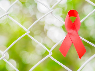 世界艾滋病日的概念。红丝带挂在金属网和树上的叶子散景背景