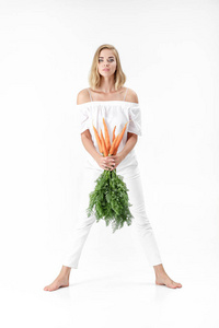 漂亮的金发女郎，拿着绿色的新鲜胡萝卜叶在白色背景上。健康与饮食