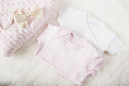 一个女孩的婴儿衣服。宝宝连体裤 连裤 弓发带和粉红色的尿布。在白色的皮毛的地毯上。刚出生的婴儿的概念。宝贝女孩衣服套