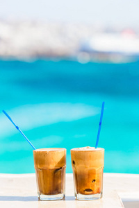 冰沙，冰咖啡在海滩上的。夏季冰咖啡星冰乐 冰沙或拿铁咖啡在高大的玻璃背景在海滩酒吧海