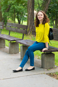 美丽的时尚女孩坐在公园长椅上的肖像