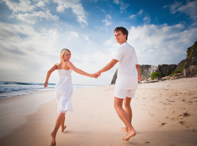 新婚夫妇穿着白色衣服在海滩上跑步