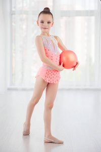 漂亮的小体操运动员女孩粉红色的运动装打扮，表演艺术体操元素与球健身班